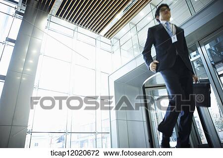 Stock Image - A business man with a briefcase man running into an office building . Fotosearch