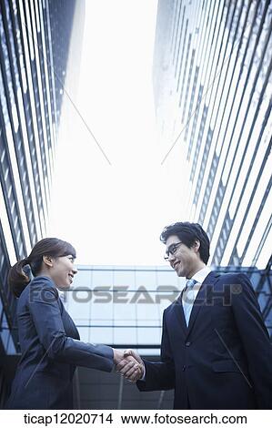 Picture - A business man with a briefcase shacking hands with a business woman . Fotosearch
