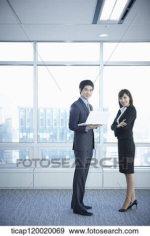 A business woman and a man standing in front of windows while man holding a laptop View Large Photo Image Stock Photo - A business woman and a man standing in front of windows while man holding a laptop. Fotosearch