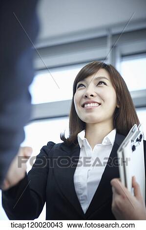 Stock Image - A business woman smiling while shaking hands with a holder in her arms. Fotosearch