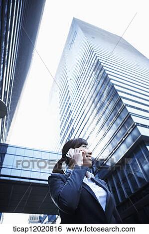 A business woman talking on a mobile phone and waving between office buildings View Large Photo Image Stock Photograph - A business woman talking on a mobile phone and waving between office buildings. Fotosearch