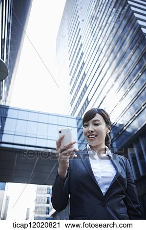 Stock Image - A business woman using a smart phone between office buildings. Fotosearch