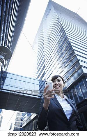 A business woman using a smart phone between office buildings View Large Photo Image Stock Image - A business woman using a smart phone between office buildings. Fotosearch