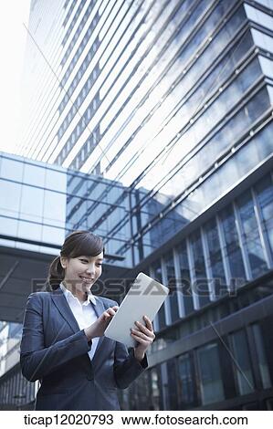 Stock Image - A business woman using a tablet device between office buildings. Fotosearch