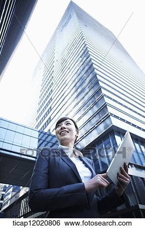 A business woman using a tablet device between office buildings View Large Photo Image Stock Photograph - A business woman using a tablet device between office buildings. Fotosearch