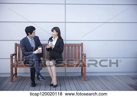 A businessman and businesswoman sitting on a bench drinking coffee View Large Photo Image Stock Photo - A businessman and businesswoman sitting on a bench drinking coffee. Fotosearch