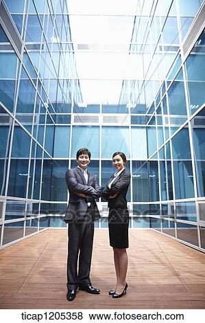 A businessman and woman standing with their arms crossed in a modern building View Large Photo Image Stock Photo - A businessman and woman standing with their arms crossed in a modern building. Fotosearch
