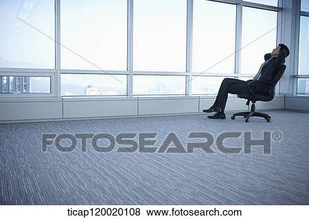 A businessman leaning back on a chair next to huge windows View Large Photo Image Stock Photo - A businessman leaning back on a chair next to huge windows. Fotosearch