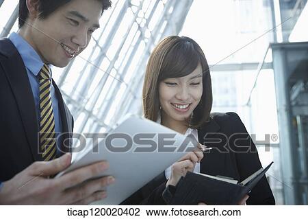 A businessman looking at a report while businesswoman checks her sheduler View Large Photo Image Stock Image - A businessman looking at a report while businesswoman checks her sheduler. Fotosearch