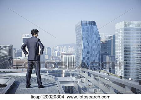 A businessman looking down the city with arms on his waist View Large Photo Image Picture - A businessman looking down the city with arms on his waist. Fotosearch