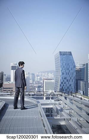 Stock Image - A businessman looking down the city while standing on a rooftop . Fotosearch