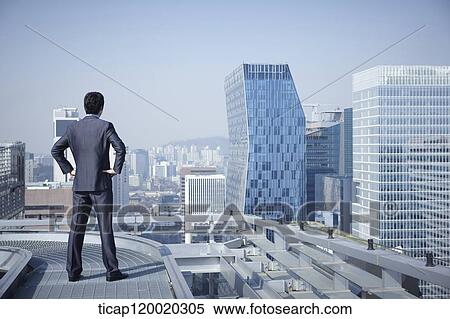 A businessman looking down the city standing on rooftop with arms on his waist View Large Photo Image Stock Photography - A businessman looking down the city standing on rooftop with arms on his waist. Fotosearch