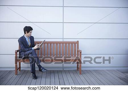 A businessman sitting on a bench doing pad View Large Photo Image Picture - A businessman sitting on a bench doing pad. Fotosearch