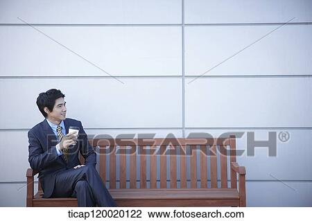 A businessman sitting on a bench drinking coffee View Large Photo Image Stock Image - A businessman sitting on a bench drinking coffee. Fotosearch