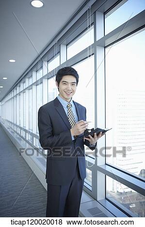 A businessman smiling while holding a diary in his hand next to a window View Large Photo Image Stock Photo - A businessman smiling while holding a diary in his hand next to a window. Fotosearch