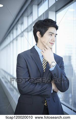 Stock Image - A businessman standing with a hand on his chin. Fotosearch
