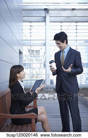 A businesswoman sitting on a bench discussing with a businessman View Large Photo Image Stock Photograph - A businesswoman sitting on a bench discussing with a businessman. Fotosearch