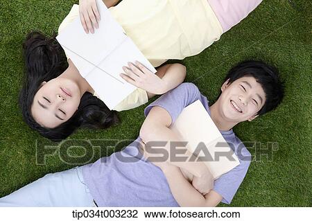 Stock Image - a couple lying on the ground and holding books. Fotosearch