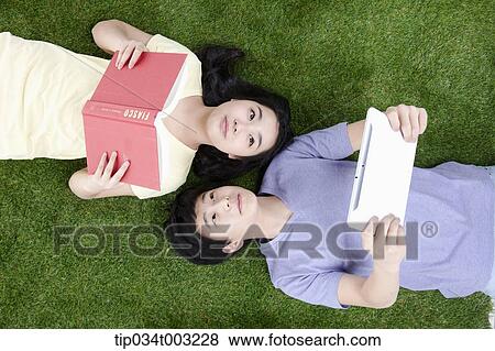 a couple lying on the ground with a book and tablet PC View Large Photo Image Stock Photo - a couple lying on the ground with a book and tablet PC. Fotosearch
