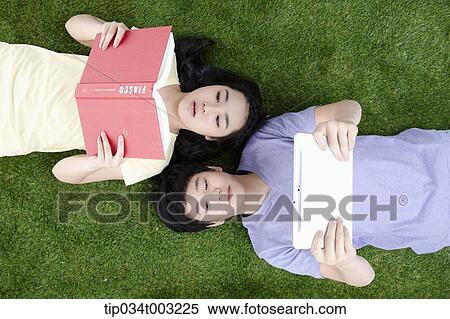 Stock Photography - a couple lying on the ground with a book and tablet PC. Fotosearch