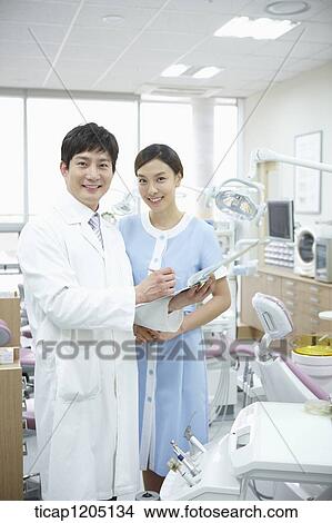 A dentist and a nurse standing in a dental treatment room View Large Photo Image Picture - A dentist and a nurse standing in a dental treatment room. Fotosearch
