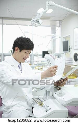A dentist going through a report in dental treatment room View Large Photo Image Stock Image - A dentist going through a report in dental treatment room. Fotosearch