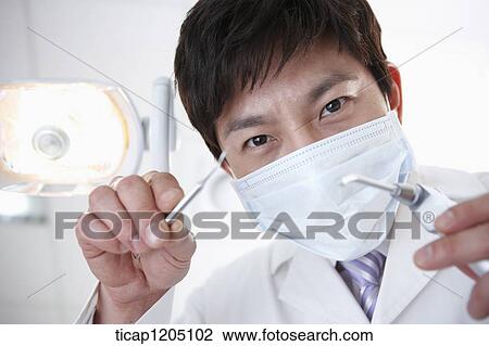 A dentist in mask using a tools under a dental light View Large Photo Image Stock Image - A dentist in mask using a tools under a dental light. Fotosearch