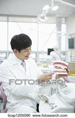 A dentist smiling while holding a false teeth in his hand in dental treatment room View Large Photo Image Stock Image - A dentist smiling while holding a false teeth in his hand in dental treatment room. Fotosearch