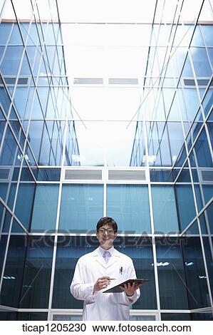 A doctor holding a report standing in middle of a modern building View Large Photo Image Stock Image - A doctor holding a report standing in middle of a modern building. Fotosearch