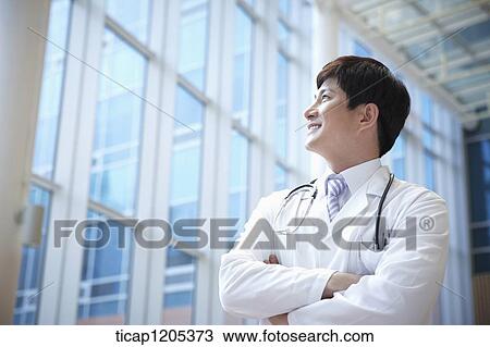 A doctor in a stethoscope around his neck standing in a building with his arms crossed View Large Photo Image Stock Image - A doctor in a stethoscope around his neck standing in a building with his arms crossed. Fotosearch