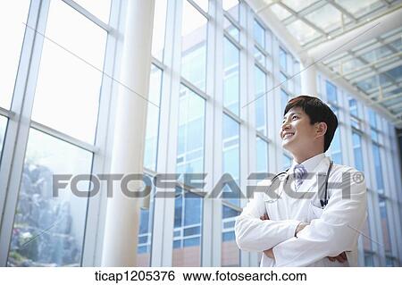A doctor in a stethoscope around his neck standing in a building with his arms crossed View Large Photo Image Stock Photograph - A doctor in a stethoscope around his neck standing in a building with his arms crossed. Fotosearch