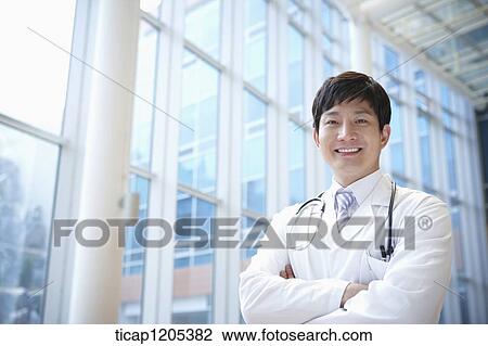 A doctor in a white dressing gown smiling at a camera with his arms crossed View Large Photo Image Stock Image - A doctor in a white dressing gown smiling at a camera with his arms crossed. Fotosearch