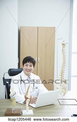 A doctor sitting in his office using his white laptop View Large Photo Image Stock Photograph - A doctor sitting in his office using his white laptop. Fotosearch