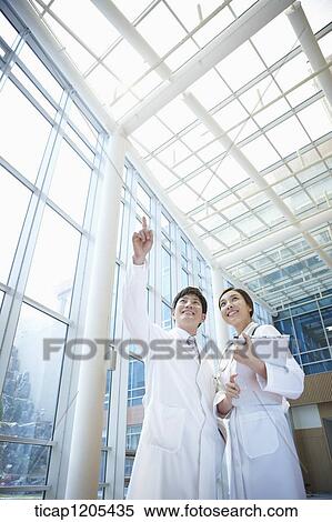 Stock Photography - A male doctor pointing while a female doctor holding a report. Fotosearch