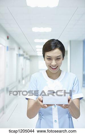 Picture - A nurse bowing while holding a present in an empty corridor. Fotosearch