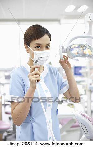 Picture - A nurse holding a dental equipment with a mask on. Fotosearch
