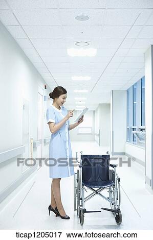A nurse looking at a report standing next to a wheelchair in hospital View Large Photo Image Stock Photo - A nurse looking at a report standing next to a wheelchair in hospital. Fotosearch