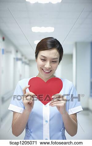 Stock Image - A nurse smiling in an empty hospital corridor holding a shape of heart. Fotosearch