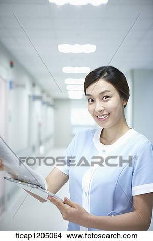 Picture - A nurse standing in an empty hospital corridor reading a report. Fotosearch