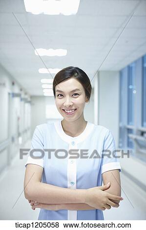 Stock Photo - A nurse standing in an empty hospital corridor with her arms crossed. Fotosearch