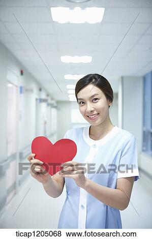 A nurse standing in an empty hospital corridor holding a shape of heart View Large Photo Image Stock Photo - A nurse standing in an empty hospital corridor holding a shape of heart. Fotosearch