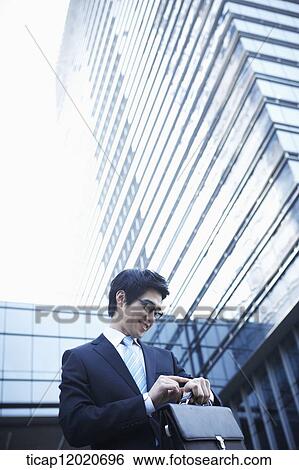 Stock Photograph - A smiling business man walking between office buildings checking the time on his watch. Fotosearch