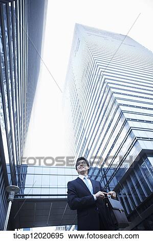 A smiling business man walking between office buildings with a briefcase looking around View Large Photo Image Stock Photography - A smiling business man walking between office buildings with a briefcase looking around. Fotosearch