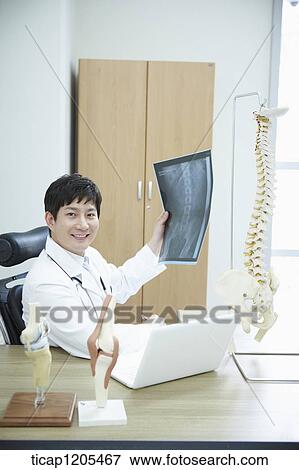 A surgeon smiling on his chair with a x-ray result in his hand and spine model on his desk View Large Photo Image Stock Photo - A surgeon smiling on his chair with a x-ray result in his hand and spine model on his desk. Fotosearch