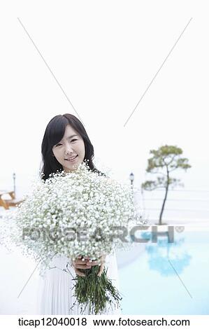 Stock Photo - A woman holding a bucay of with flowers with a tree in the backgound. Fotosearch
