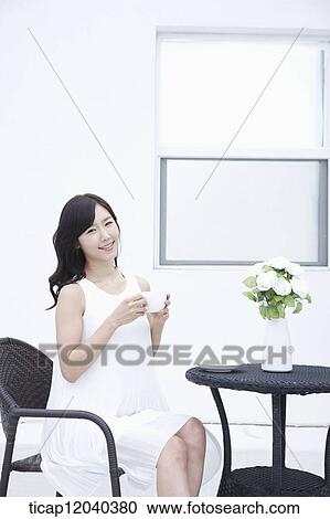 A woman in a white dress and a coffee cup in her hand sitting on black garden furniture View Large Photo Image Stock Image - A woman in a white dress and a coffee cup in her hand sitting on black garden furniture. Fotosearch