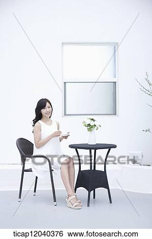 A woman in a white dress and a coffee cup in her hand sitting on black garden furniture View Large Photo Image Stock Photograph - A woman in a white dress and a coffee cup in her hand sitting on black garden furniture. Fotosearch
