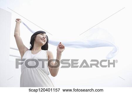 A woman in a white dress is holding a white sheet in the air with her other hand View Large Photo Image Stock Photo - A woman in a white dress is holding a white sheet in the air with her other hand. Fotosearch
