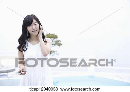 Stock Photo - A woman in white dress listening to a music. Fotosearch