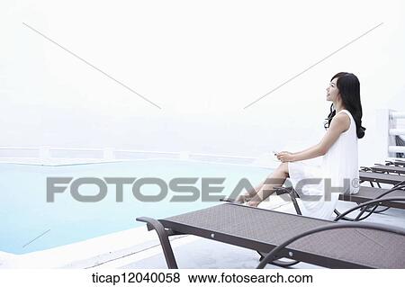A woman in white dress listening to a music on brown sunbed View Large Photo Image Stock Photo - A woman in white dress listening to a music on brown sunbed. Fotosearch